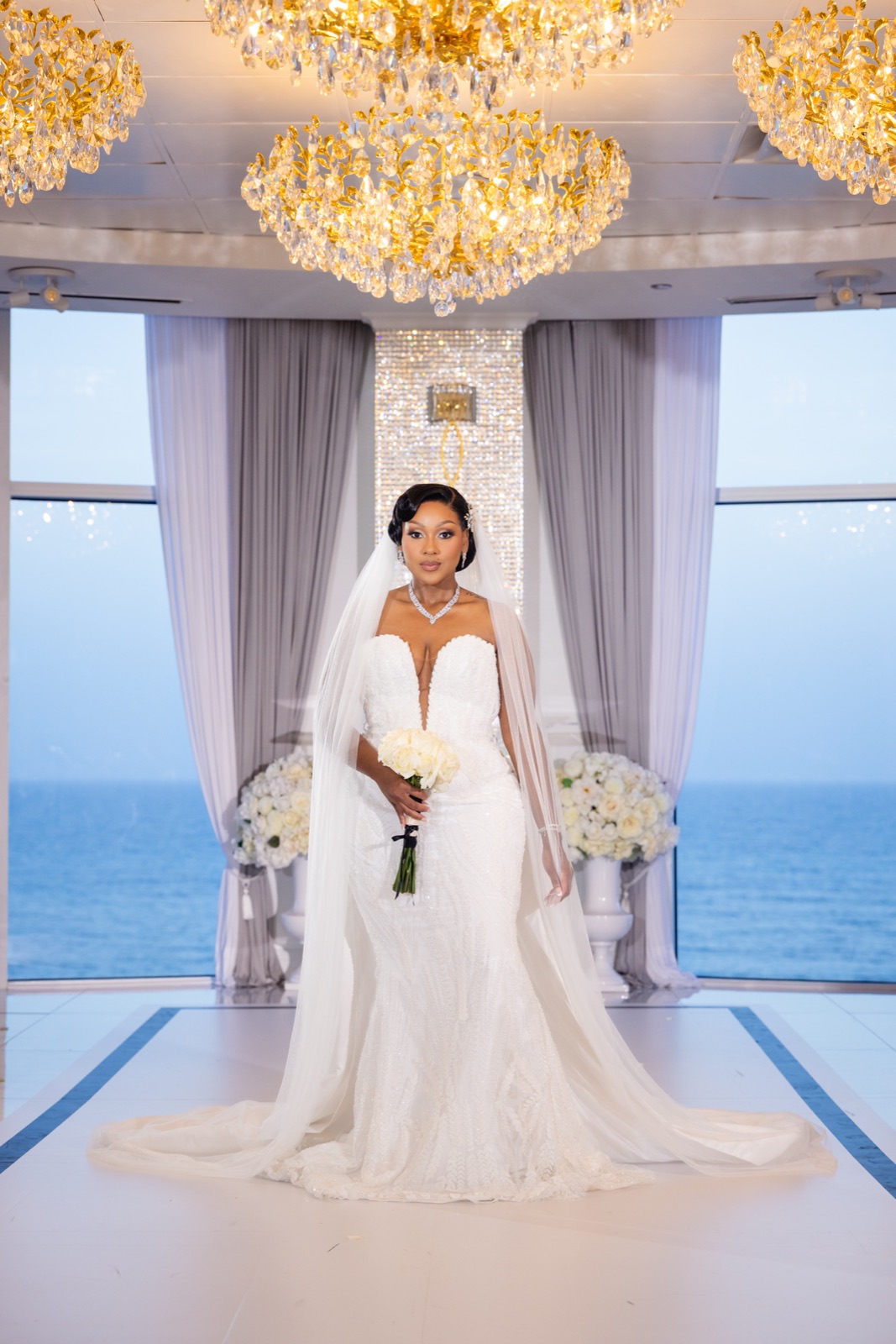 Bride beneath a grand chandelier with an ocean backdrop