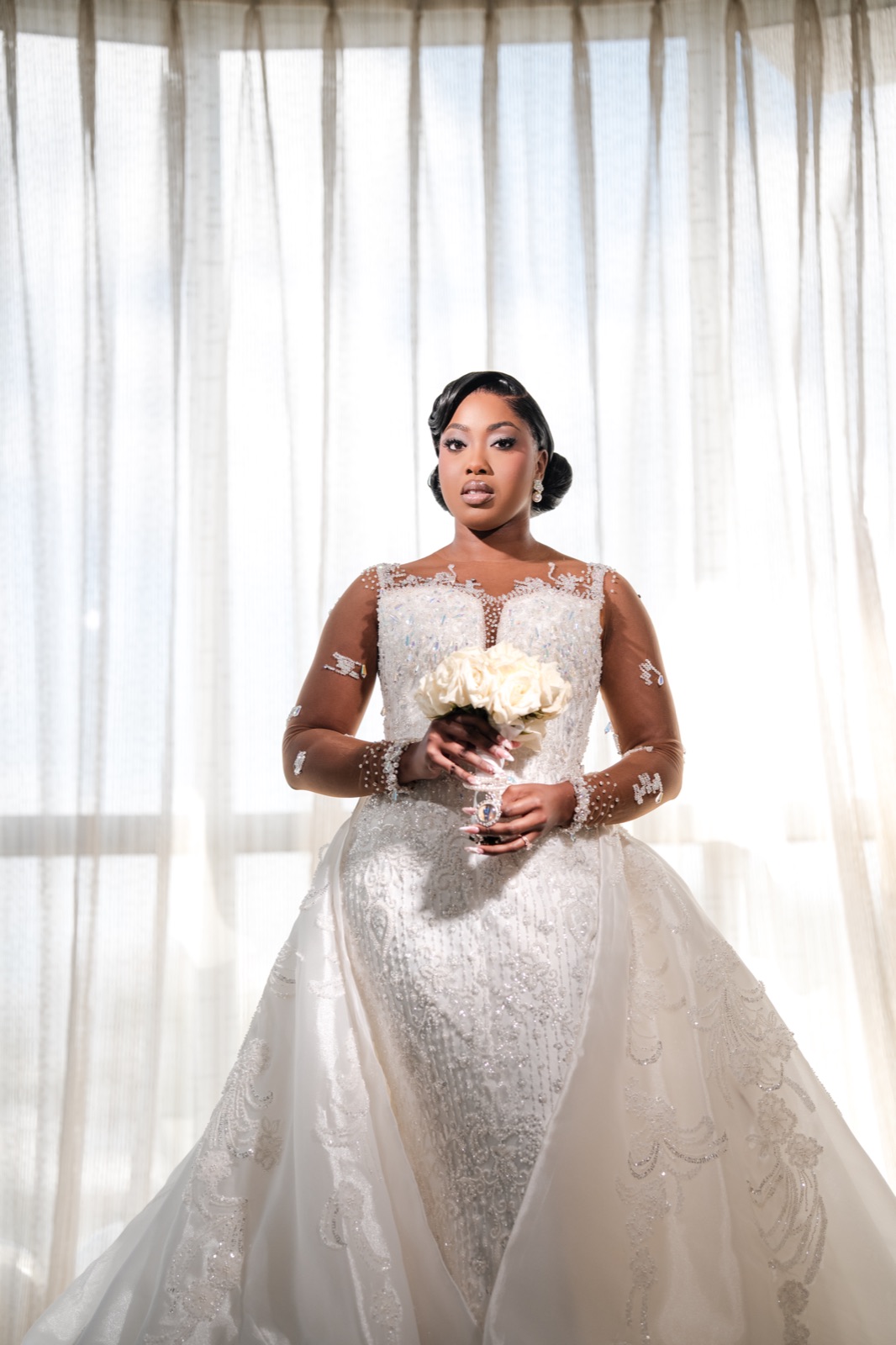 Bride in an embellished gown framed by sheer curtains